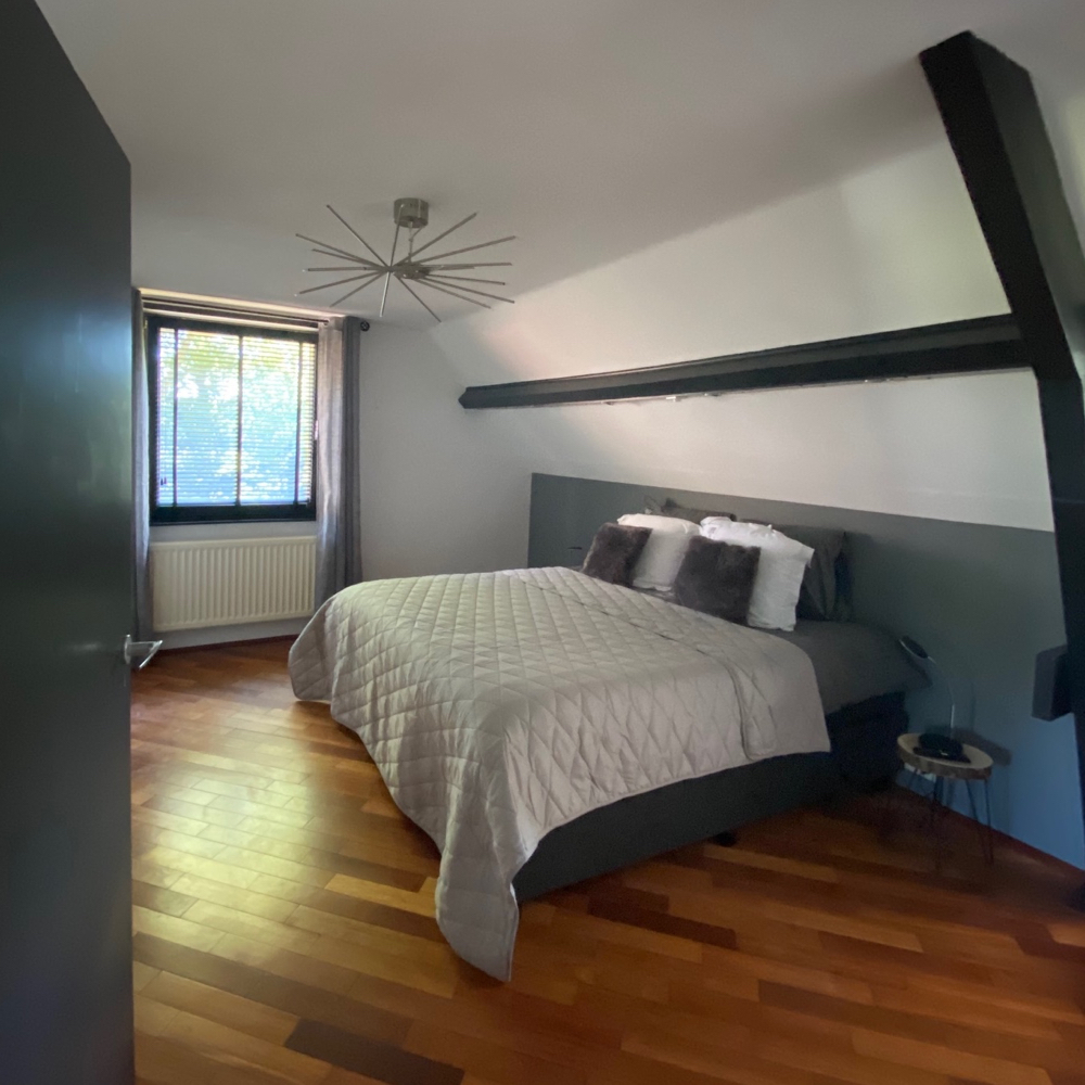 Schlafzimmer mit grauer Tagesdecke und Kissen auf dem Bett