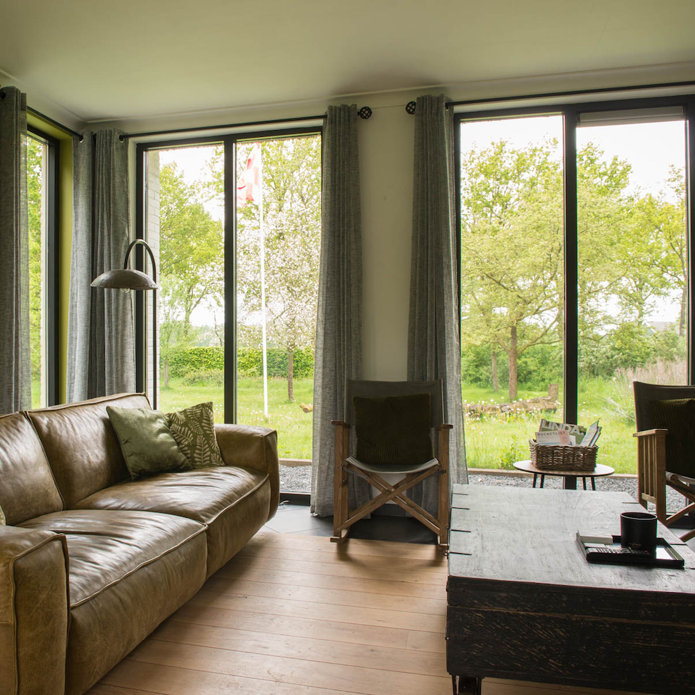 Wohnzimmer mit Sofa und großen Fenstern mit Blick auf den Garten