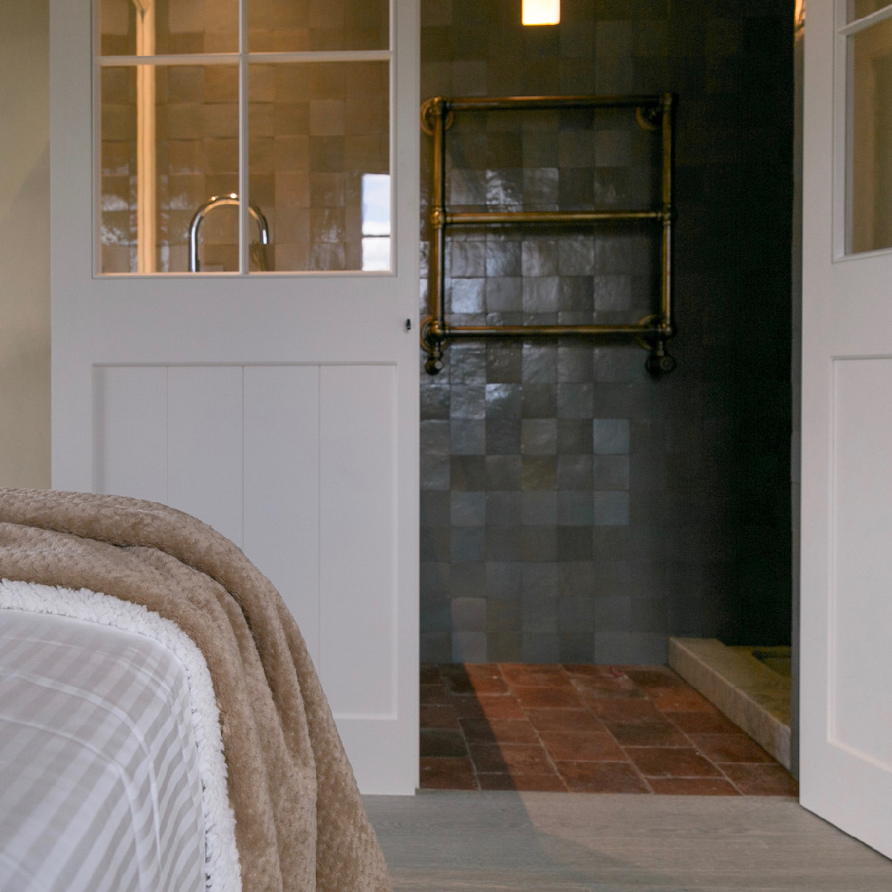 Bett mit Blick auf das Badezimmer mit grünen Fliesen und Holzschiebetür