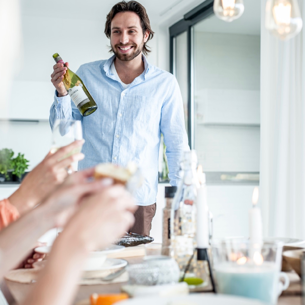 Gastgeber mit einer Flasche Wein am Esstisch
