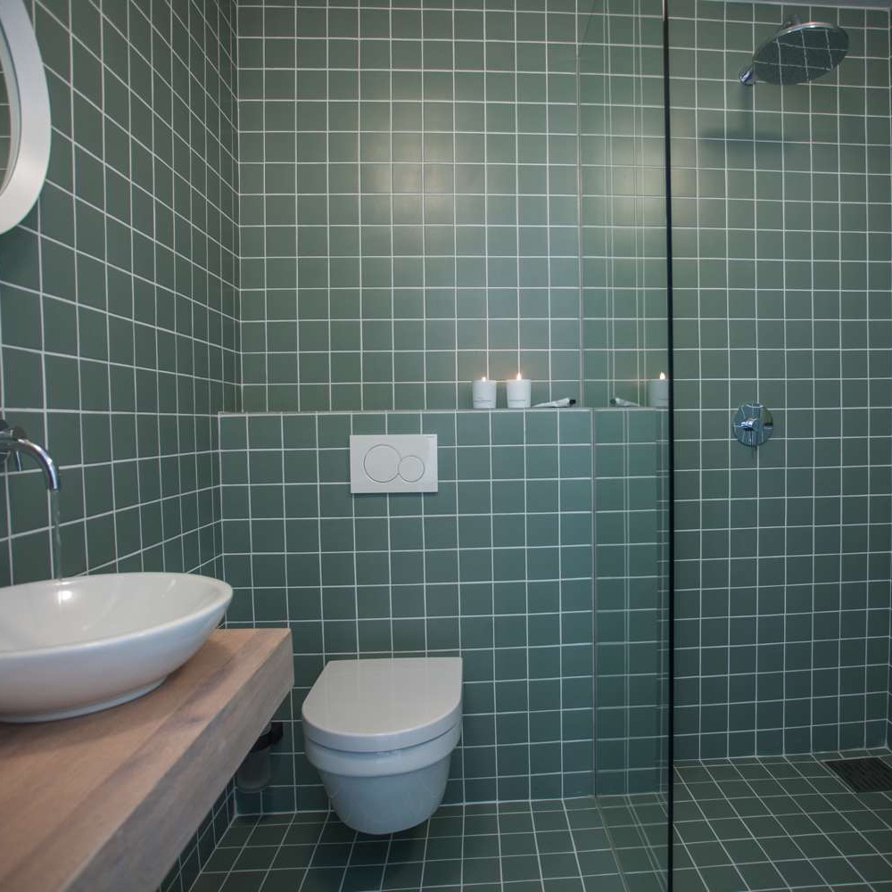 Badezimmer mit Toilette und Waschbecken und Wänden voller grüner Fliesen