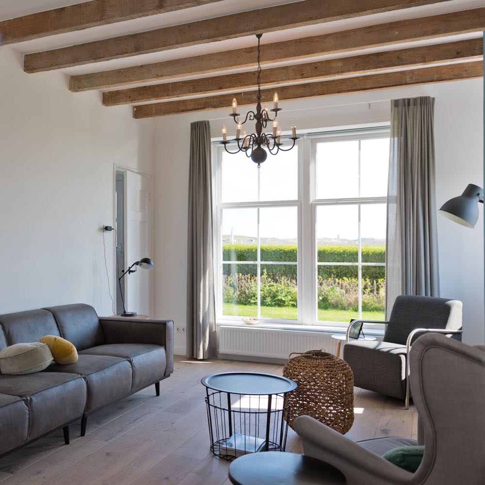 Modernes Wohnzimmer mit großen Fenstern mit Blick auf die Dünen und Wiesen