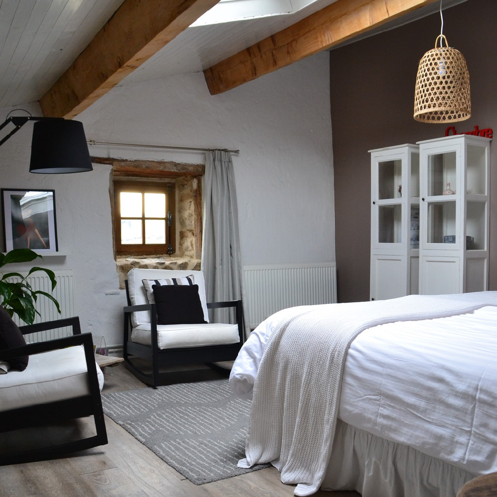 Ein Gästezimmer mit robusten Balken, weißem Kleiderschrank, weißem Bett und zwei Sesseln im Landhausstil