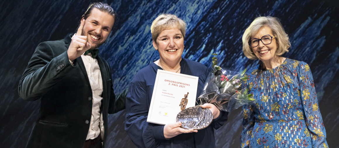 En smilende mann og to smilende kvinner på en scene