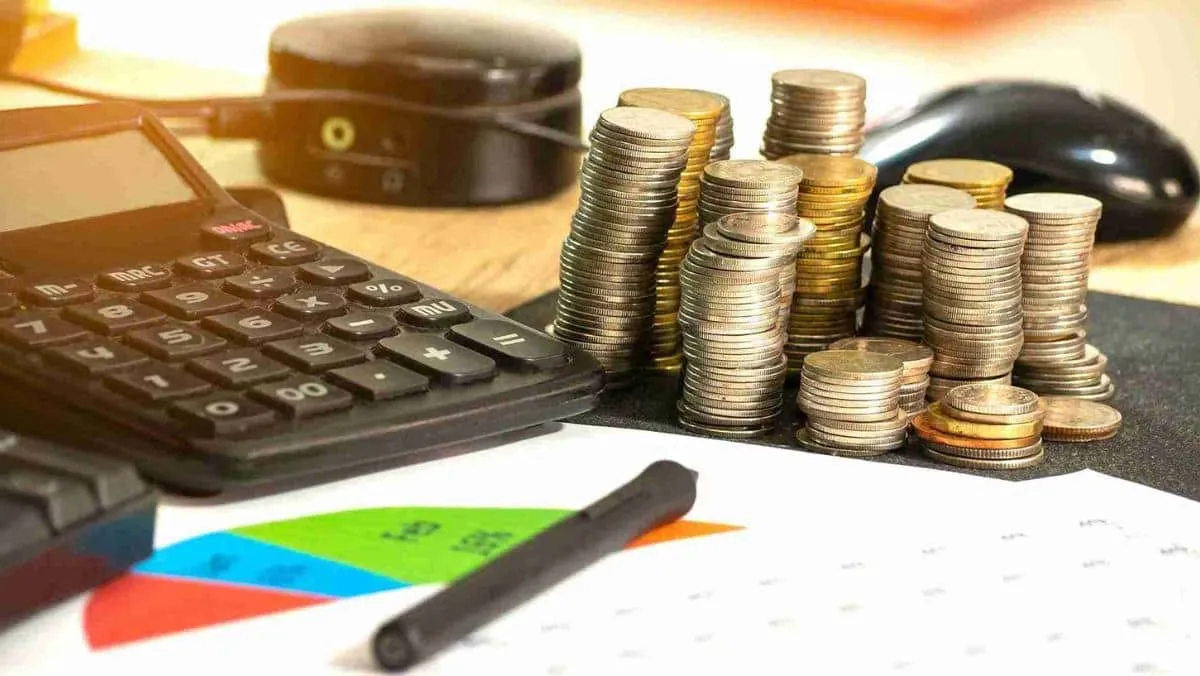 A calculator positioned alongside a stack of coins and financial documents featuring charts