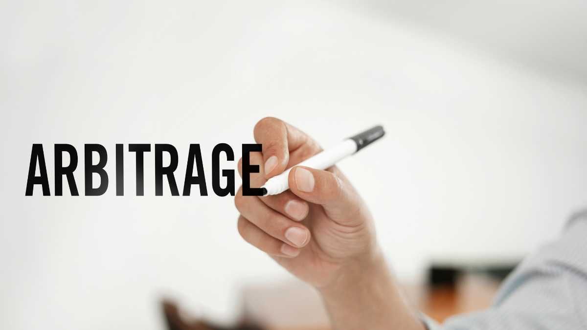 A hand holding a marker with the word ARBITRAGE written in the air