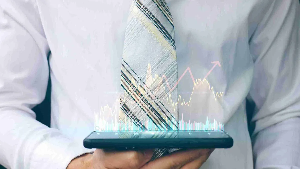 A man in a white shirt and necktie holds a mobile device, showcasing holographic trading charts