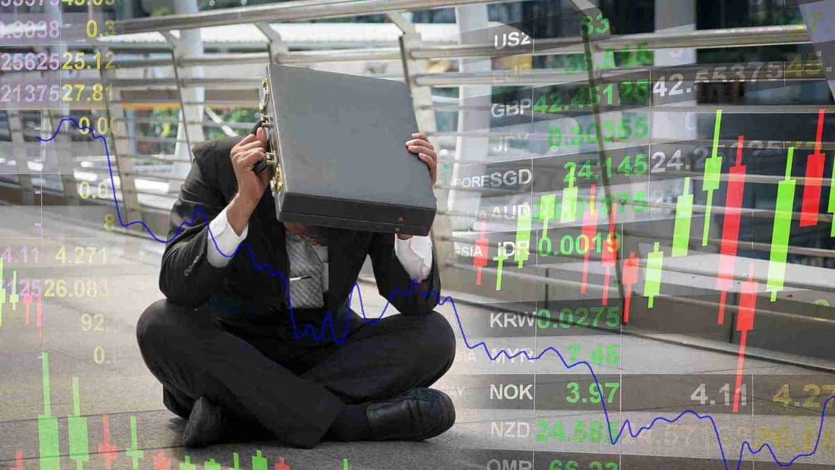 A man in formal attire sits in a hallway, his head covered by a briefcase