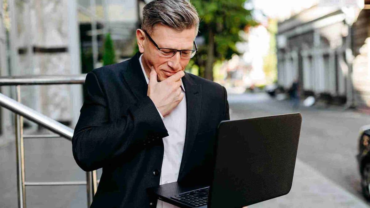 A man touching his chin with his right hand while the other hand is holding a laptop