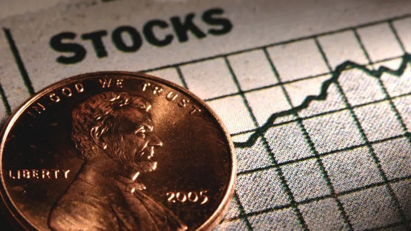 A penny coin with Abraham Lincoln's profile foregrounding a blurred chart with the word STOCKS in the background.