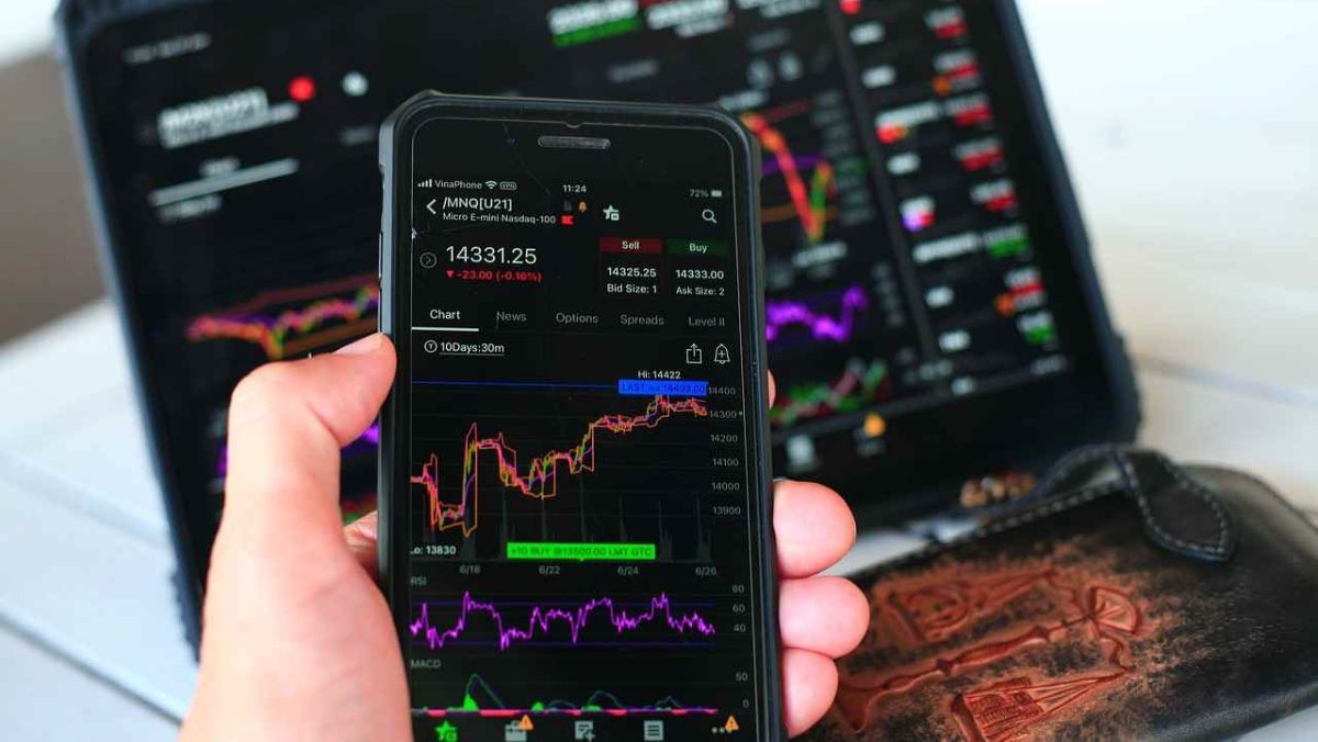 A person actively engaged in the financial market, holding a mobile device and tablet featuring live trading charts