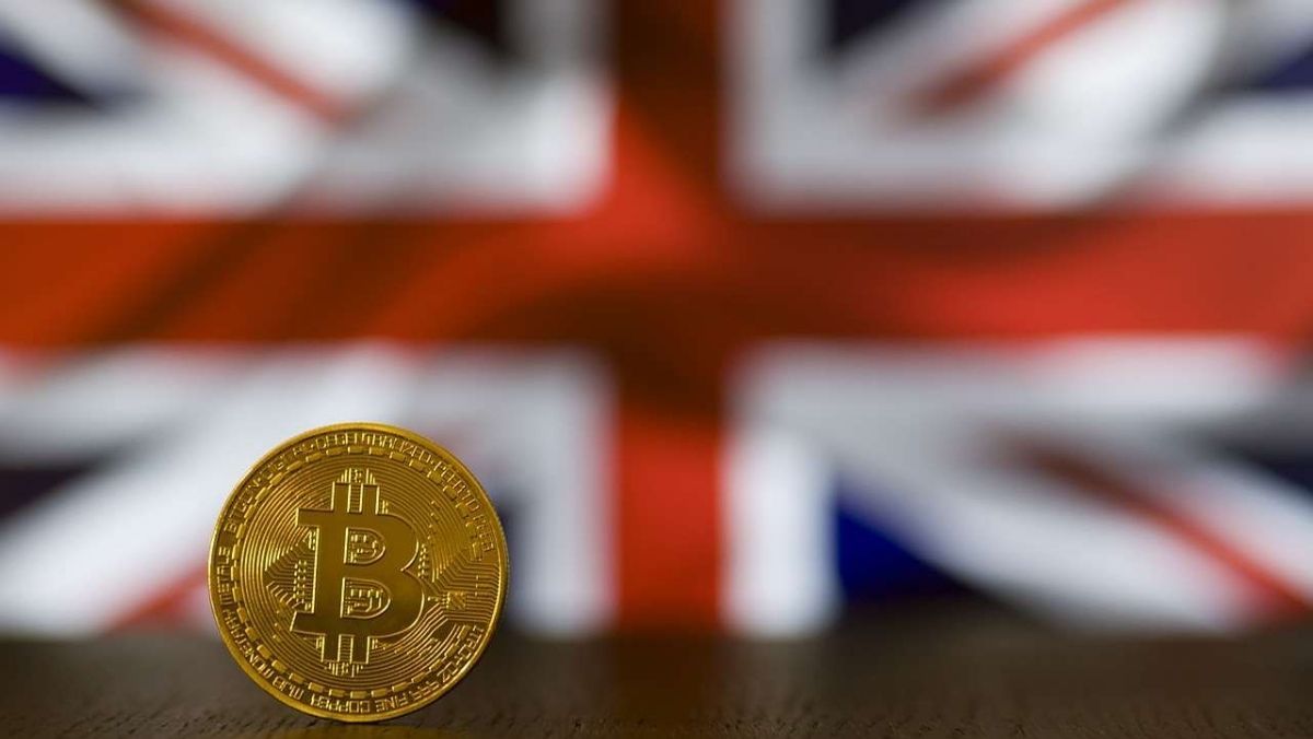 A single Bitcoin on the table and the UK flag in the background