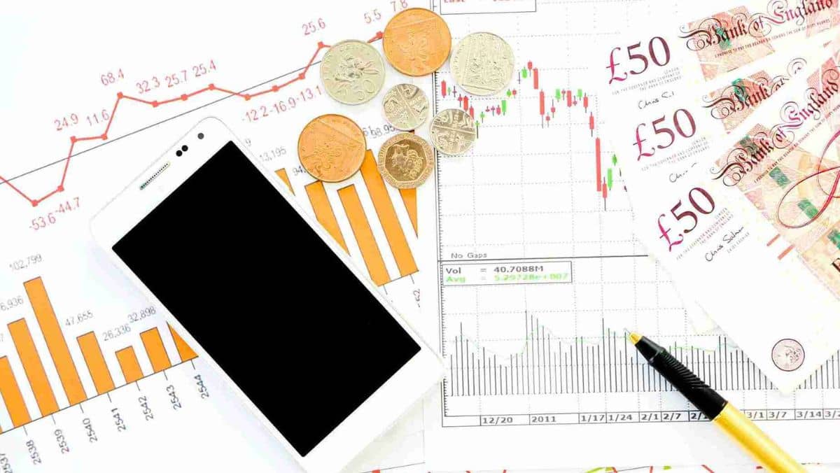 A smartphone paper bills coins and stock market documents laid out on the table