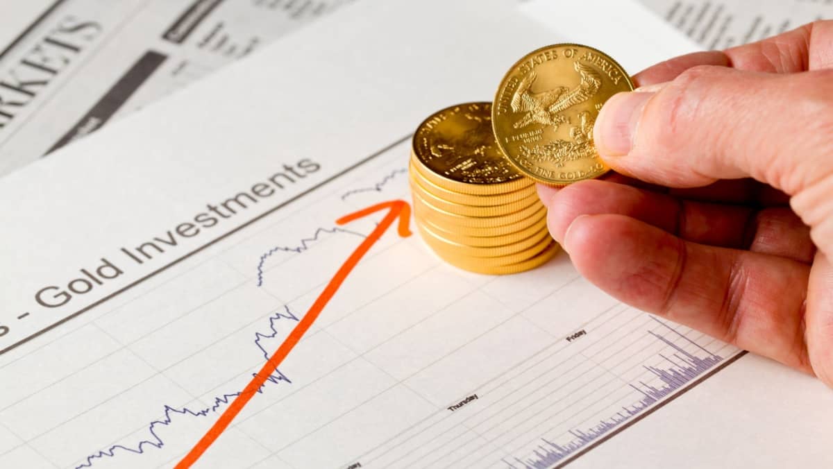 Gold Eagle one ounce coins stacked into graph of gold prices on business pages of newspaper with graphs showing increase in value and hand counting out the money
