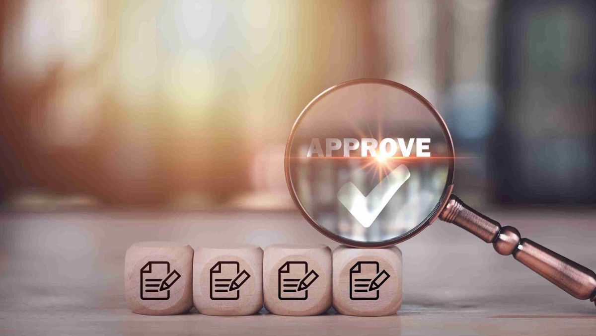 Magnifying glass with the word APPROVE alongside four wooden squares featuring logos of a document and a pen