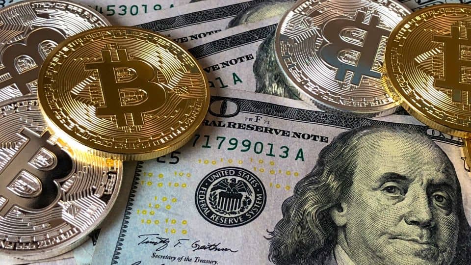 Physical Bitcoin tokens on top of US dollar bills, symbolizing the exchange between cryptocurrency and traditional currency