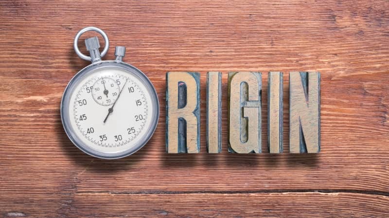 Stopwatch and the word "ORIGIN" in block letters on a wooden background