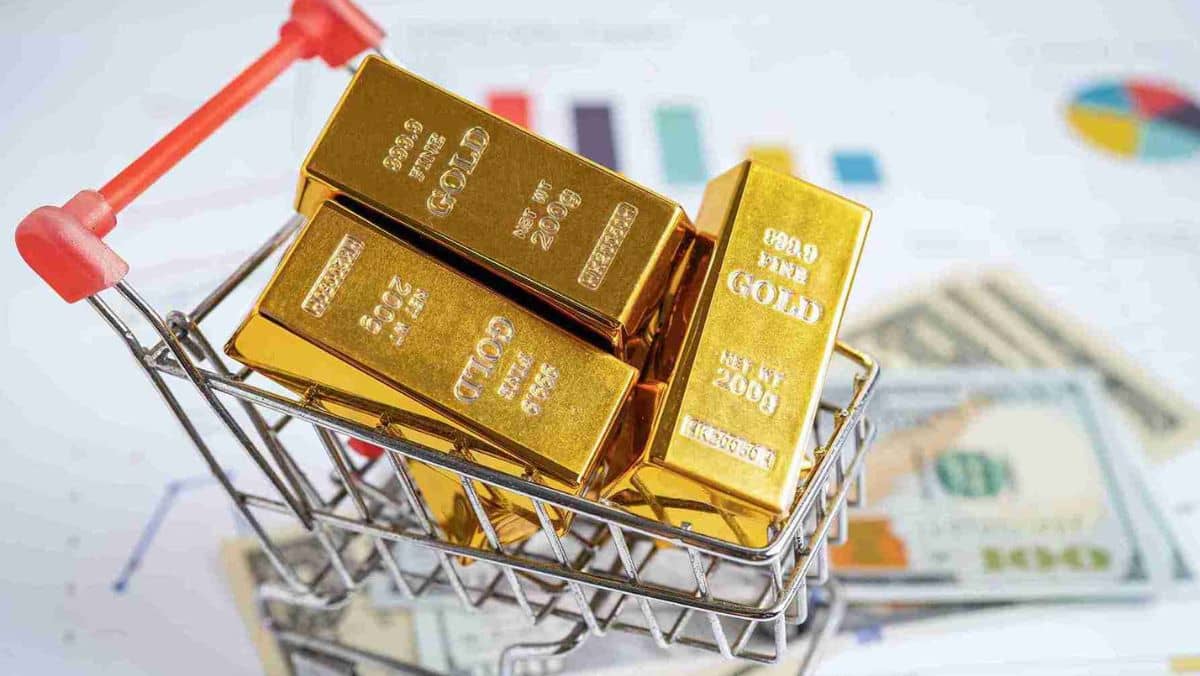 Three gold bars in a miniature shopping cart placed on a flat surface with paper documents