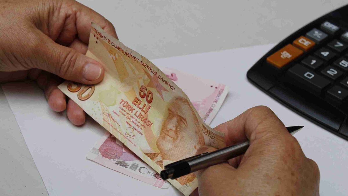 Two hands hold a Turkish Lira paper bill on the table alongside a calculator and pen