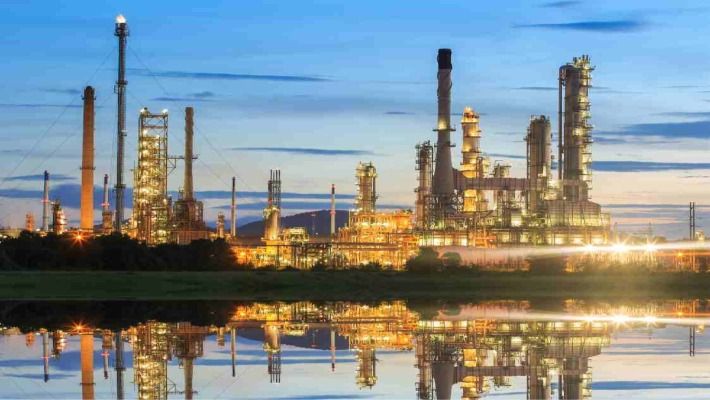 Oil refinery at dusk with lights reflected in water, showcasing industrial beauty