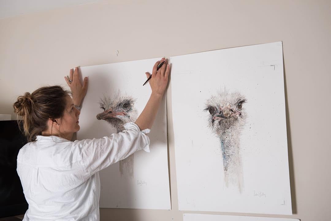 Zaza Shelley pinning large ostrich drawings to the studio wall